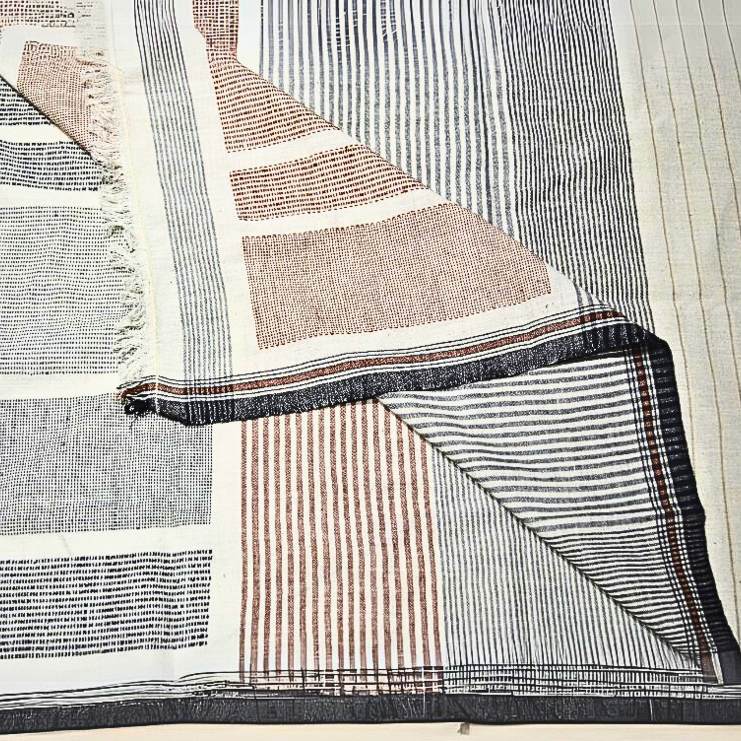 Handwoven artisanal cotton blanket with black, beige, and rust stripes, perfect for layering.