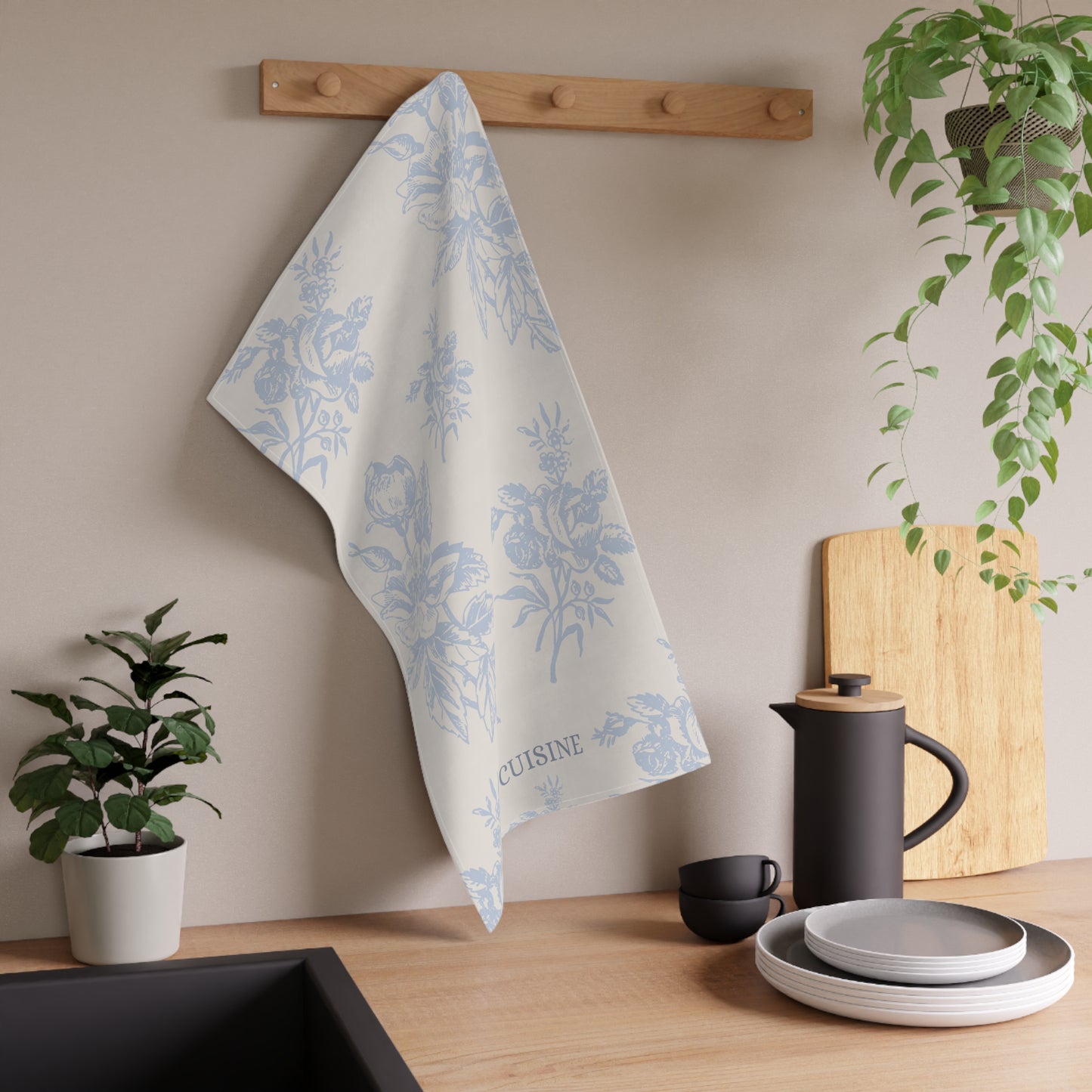 Floral towel hanging on a wooden rack above a kitchen counter with utensils and plants.