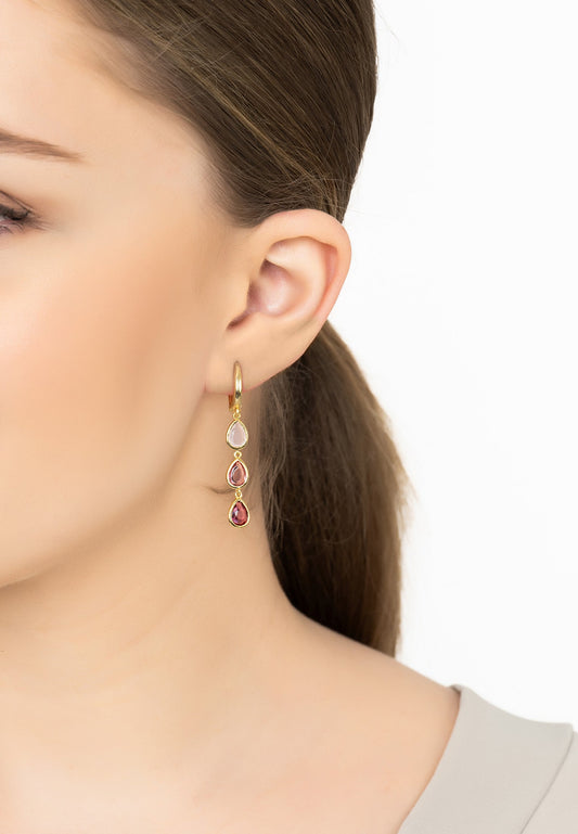 Close-up of a woman wearing gold earrings with multicolored gemstones on a white background