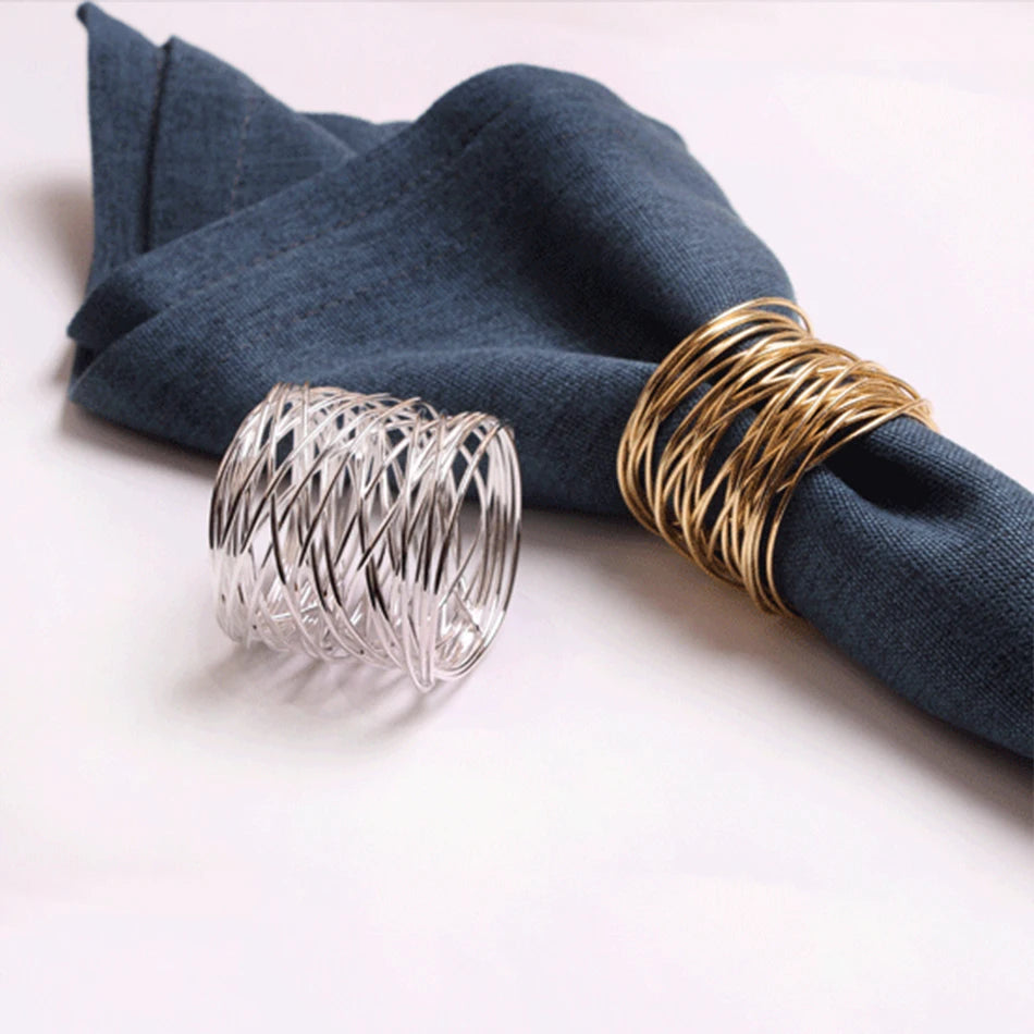 Two wire napkin rings, one silver and one gold, on a blue napkin against a white background.