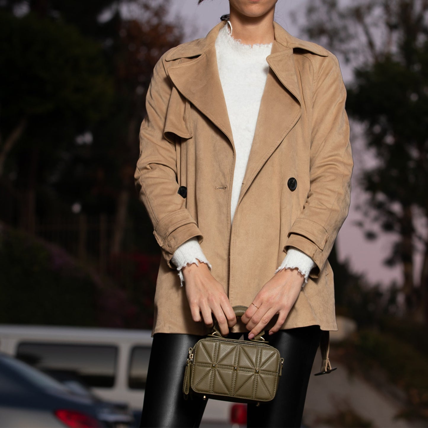 Model holding Taylor Small Quilted Crossbody Bag by the top handle styled with a camel coat