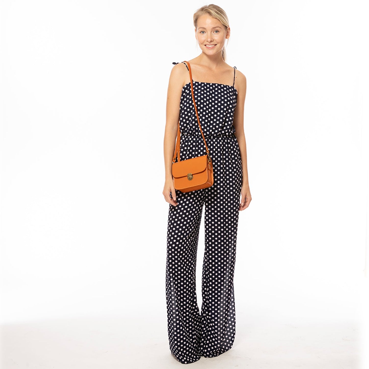 Woman wearing a polka dot jumpsuit with an orange bag on a white background