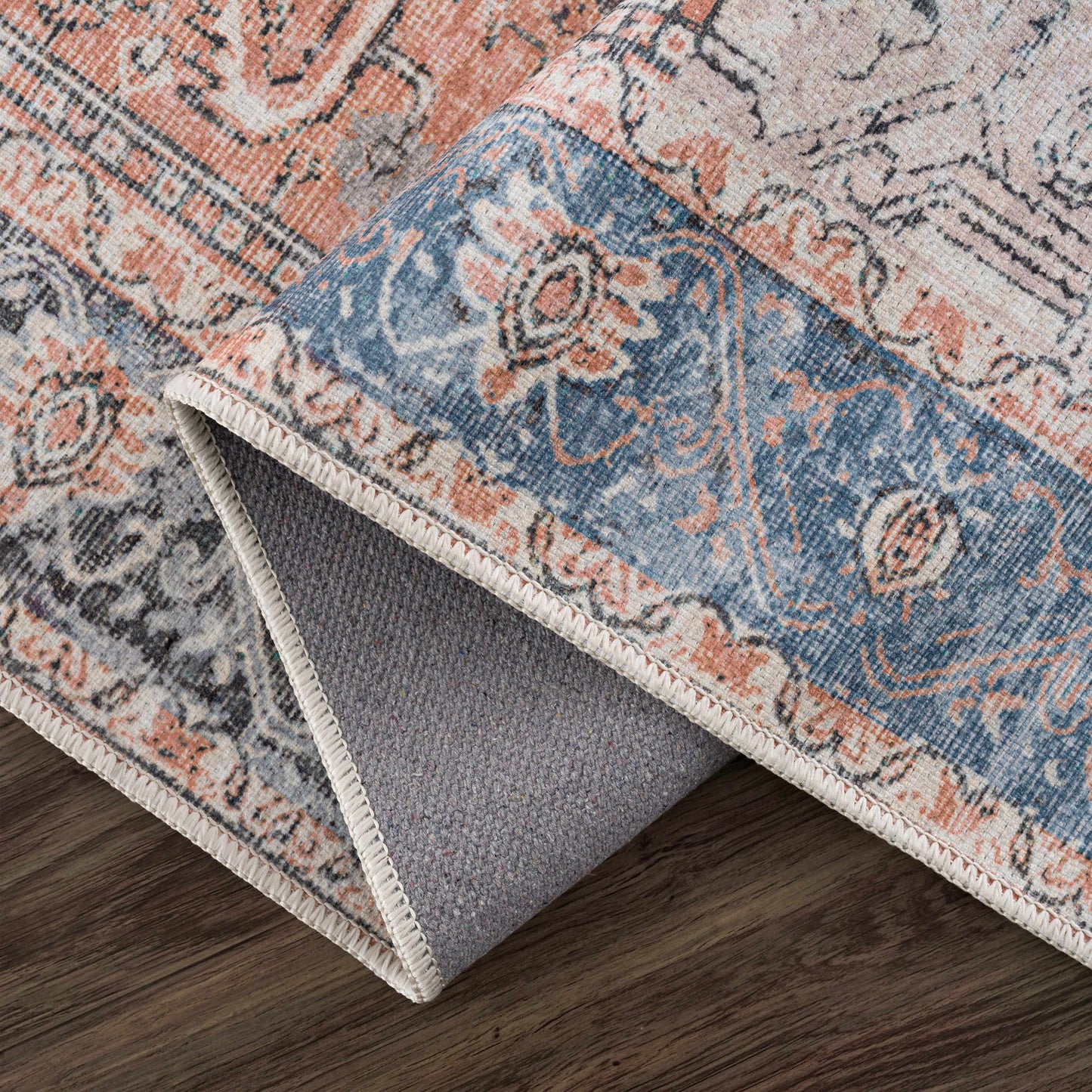 Close-up of a patterned rug with a visible transition to gray underlay on a wooden floor.