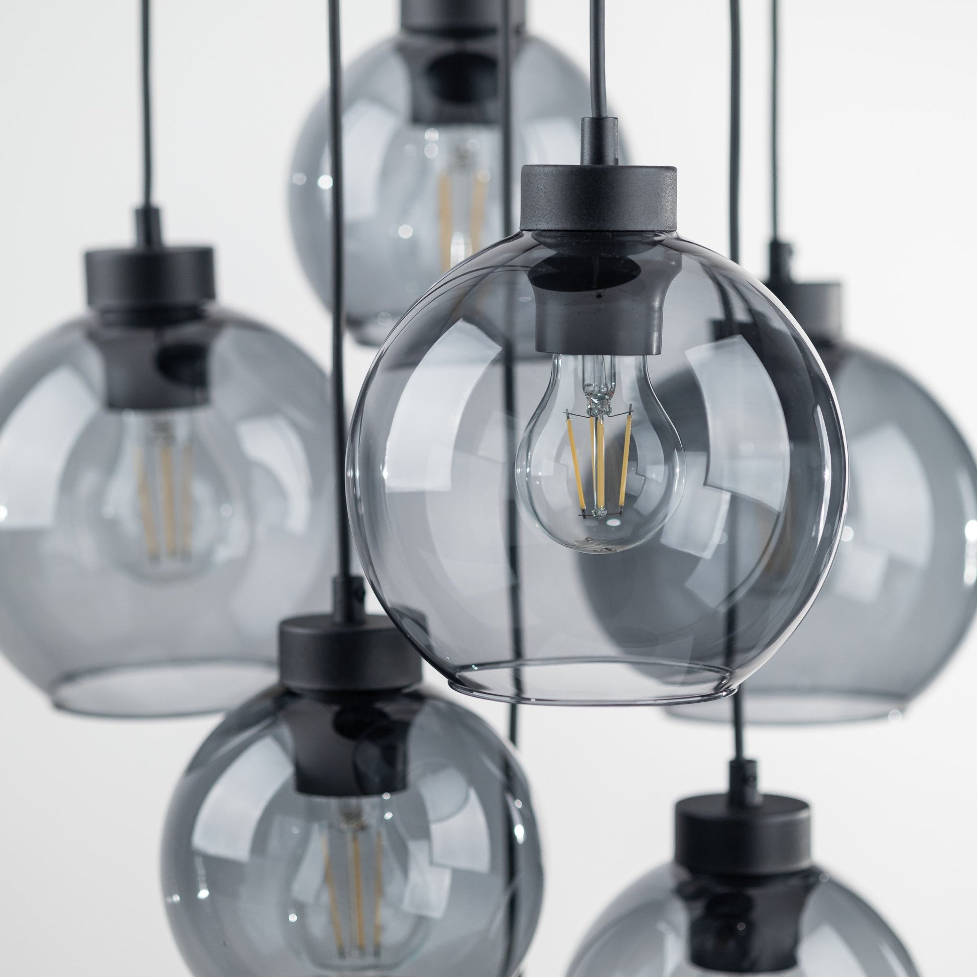 Close-up of pendant lights with clear glass shades and black metal fixtures on a light gray background.