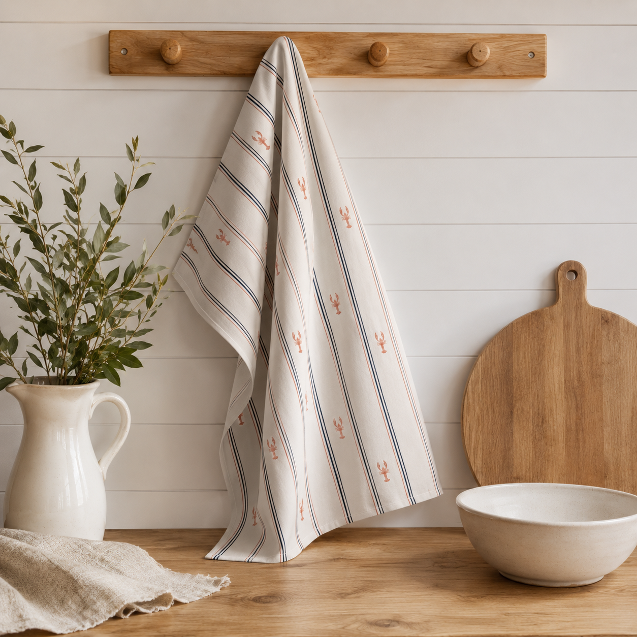 Striped towel hanging on a wooden hook with a cutting board and bowl on a wooden surface.