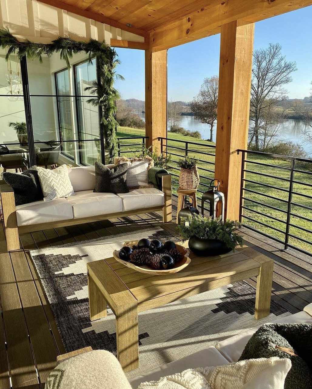 Outdoor patio with wooden furniture, cushions, and a scenic view of a lake.