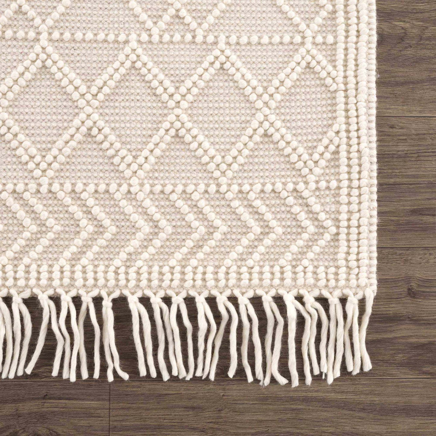 Beige woven rug with diamond pattern and white fringe on a wooden floor.