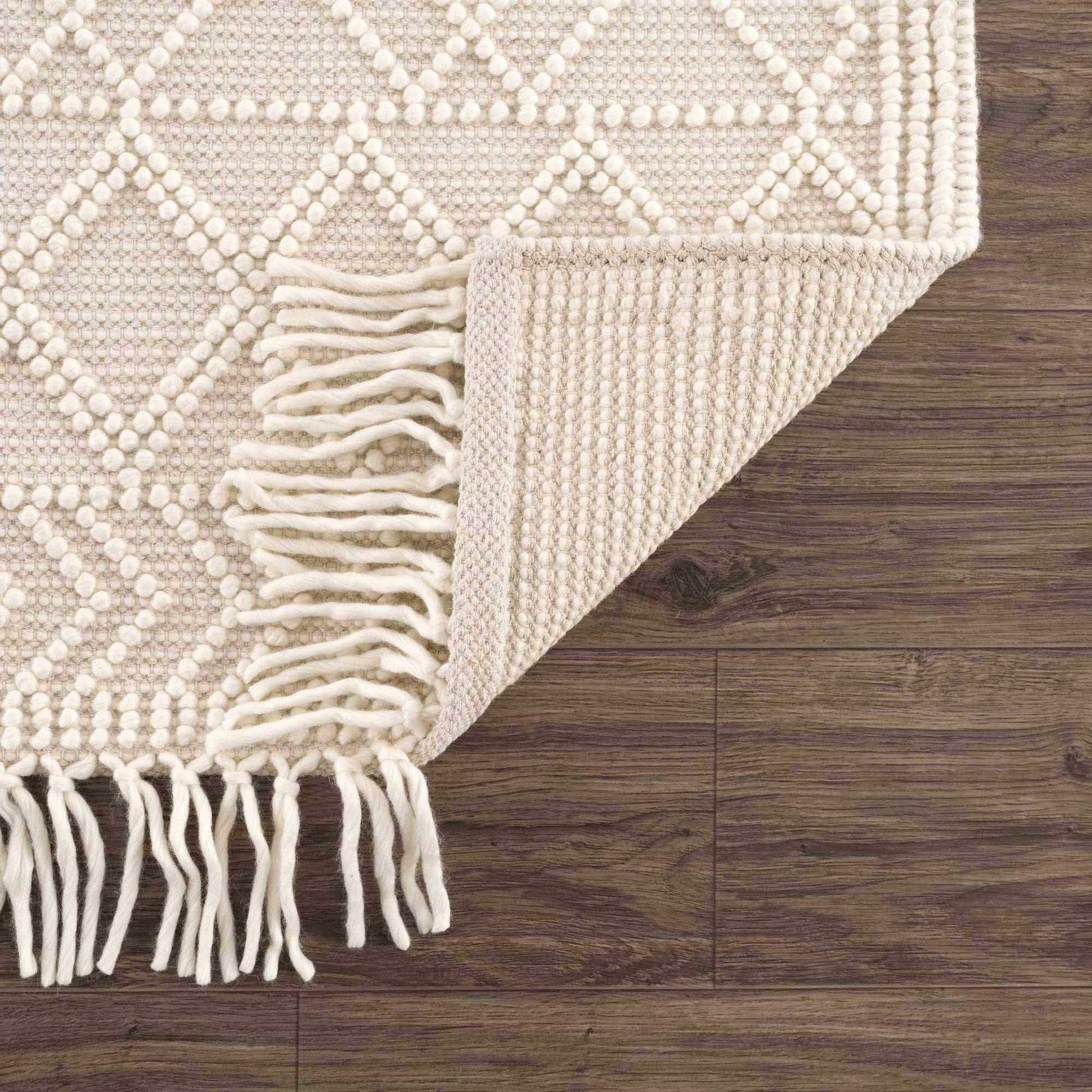 Beige textured rug with white fringe on a wooden floor