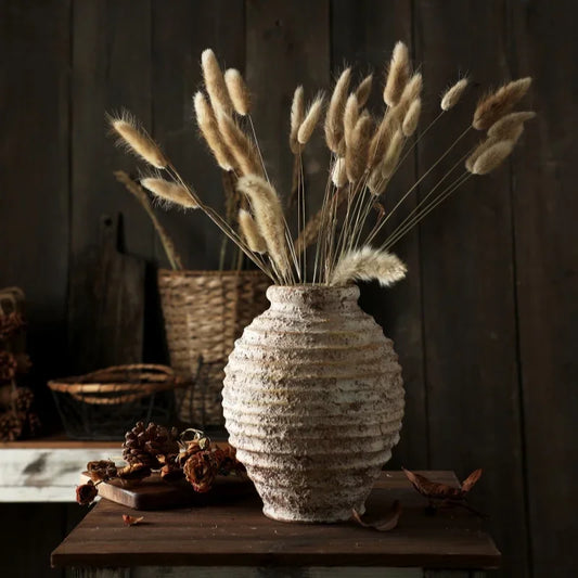 Textured vase with dried pampas grass on a wooden surface against a dark wooden wall.