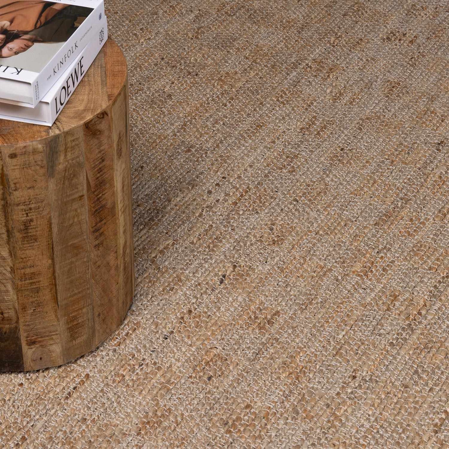 Close-up of a textured beige carpet with a wooden stool and books on it.