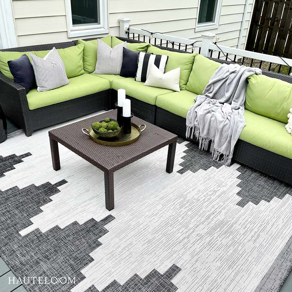 Outdoor patio with green sectional sofa, coffee table, and patterned rug.