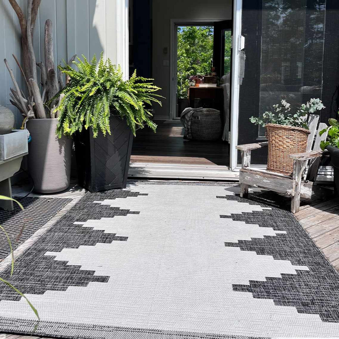 Outdoor patio with a patterned rug, potted plants, and wooden furniture.