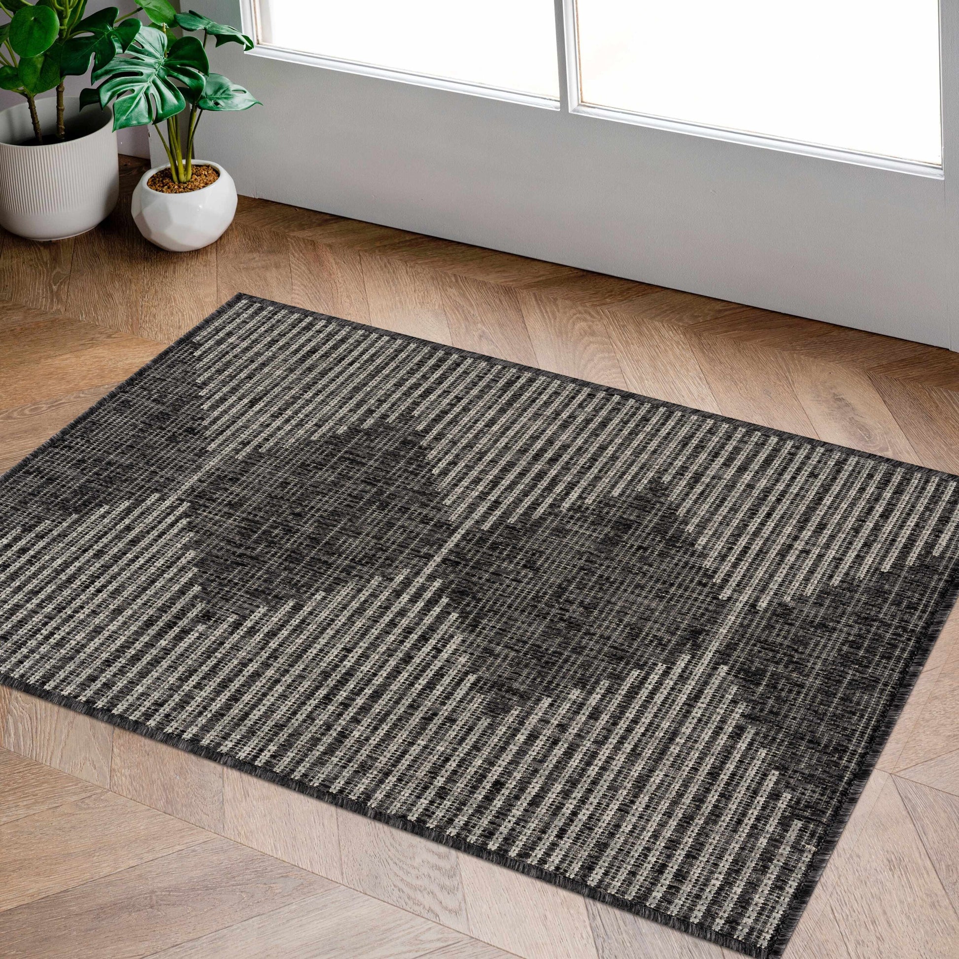 Gray patterned rug on a wooden floor with plants in the background
