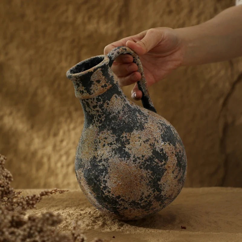 Hand holding an ancient ceramic jar against a sandy background
