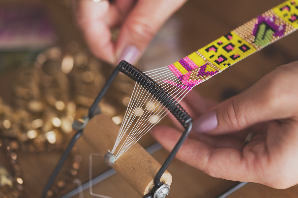 Close-up of hands using a beaded loom with colorful patterns.