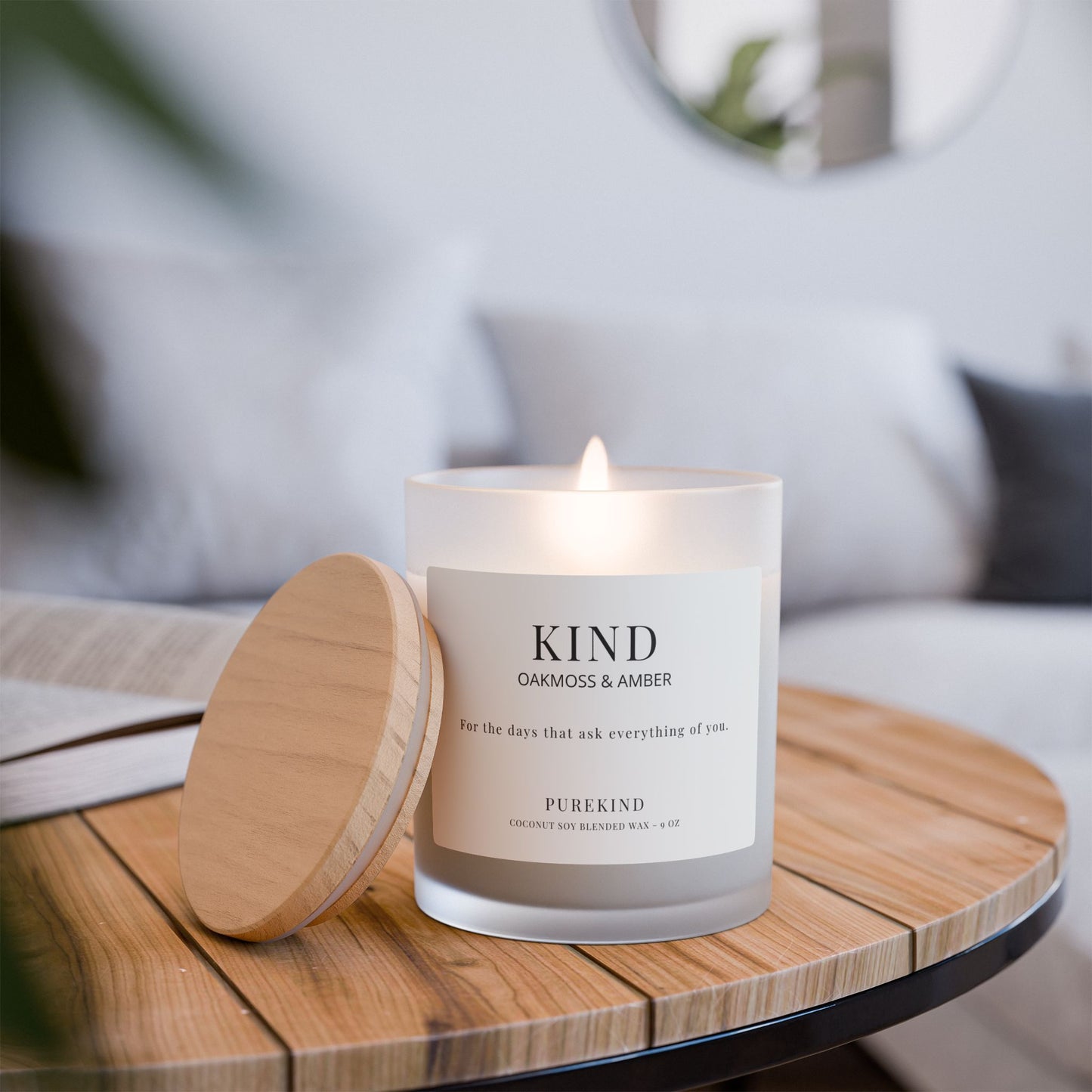 KIND oakmoss and amber candle in frosted glass jar with wood lid on table lit.