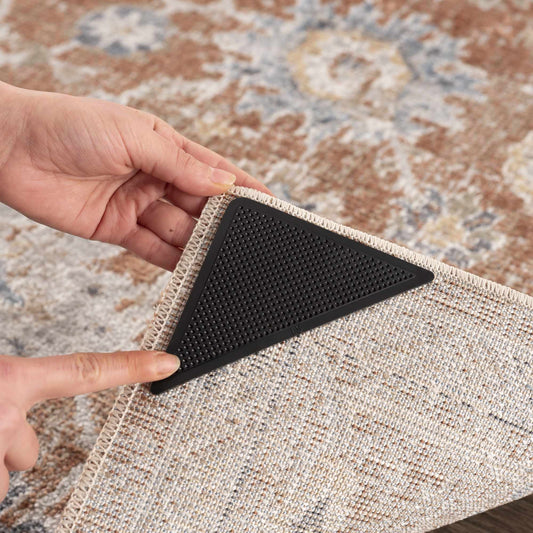 Close-up of a black triangular non-slip rug corner pad securing a rug on hardwood floor