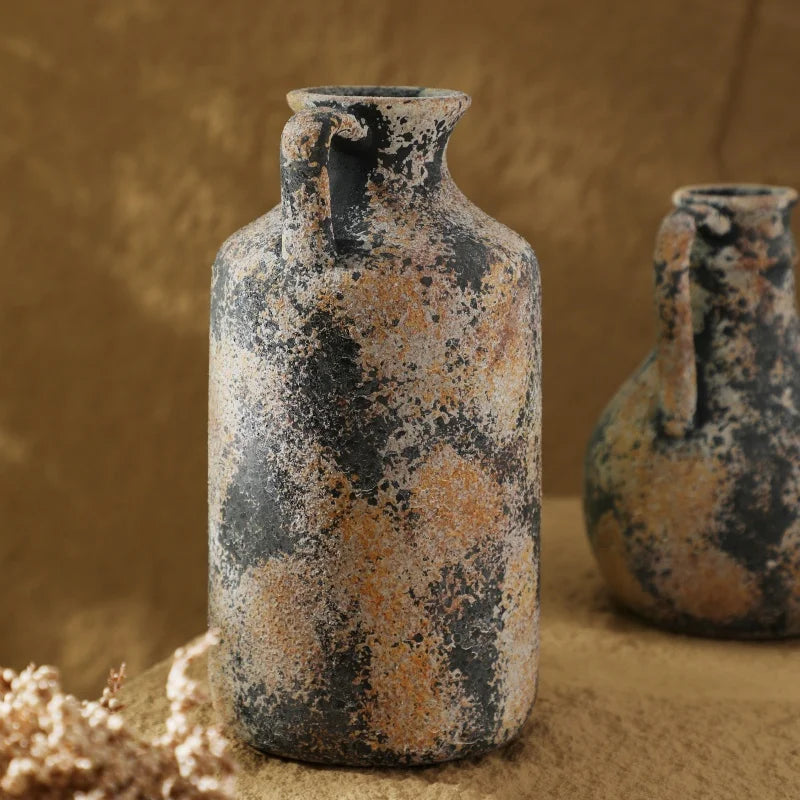 Two rustic ceramic vases with speckled glaze on a textured surface.