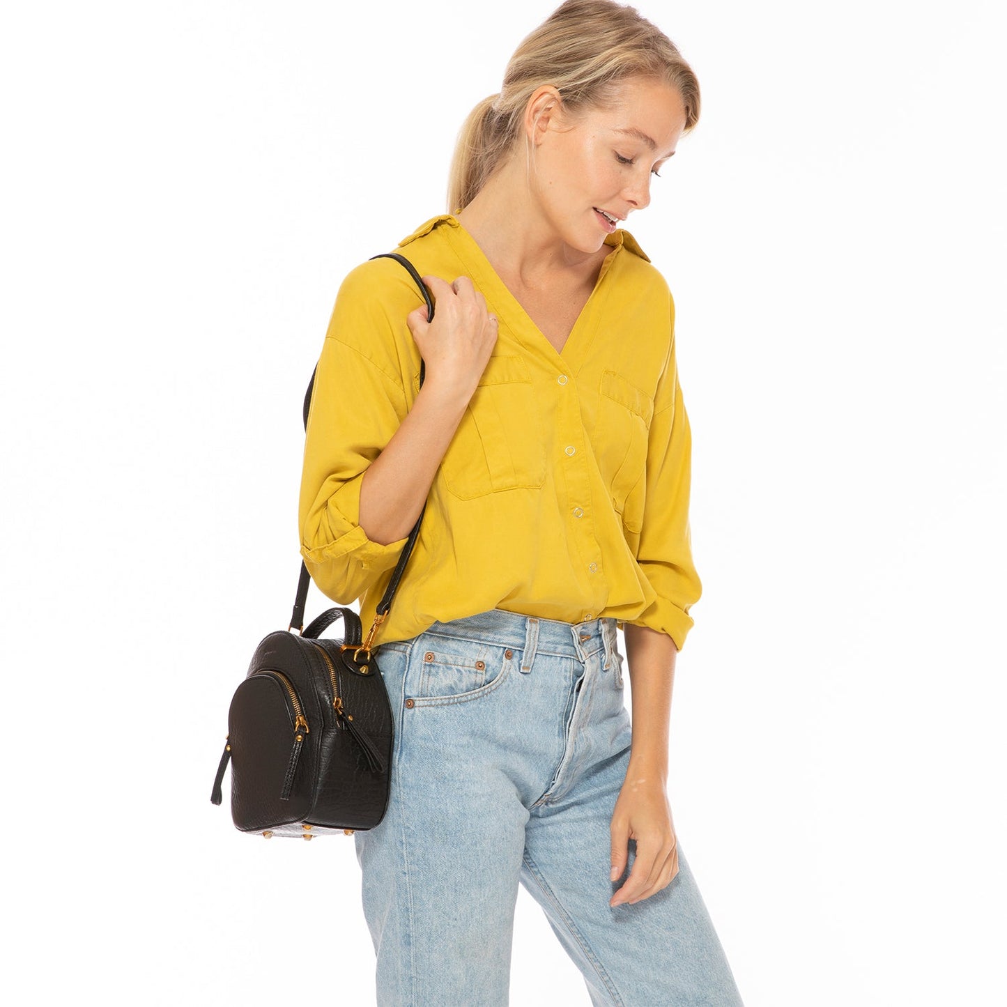 Woman wearing a yellow shirt and blue jeans, holding a black handbag on a white background