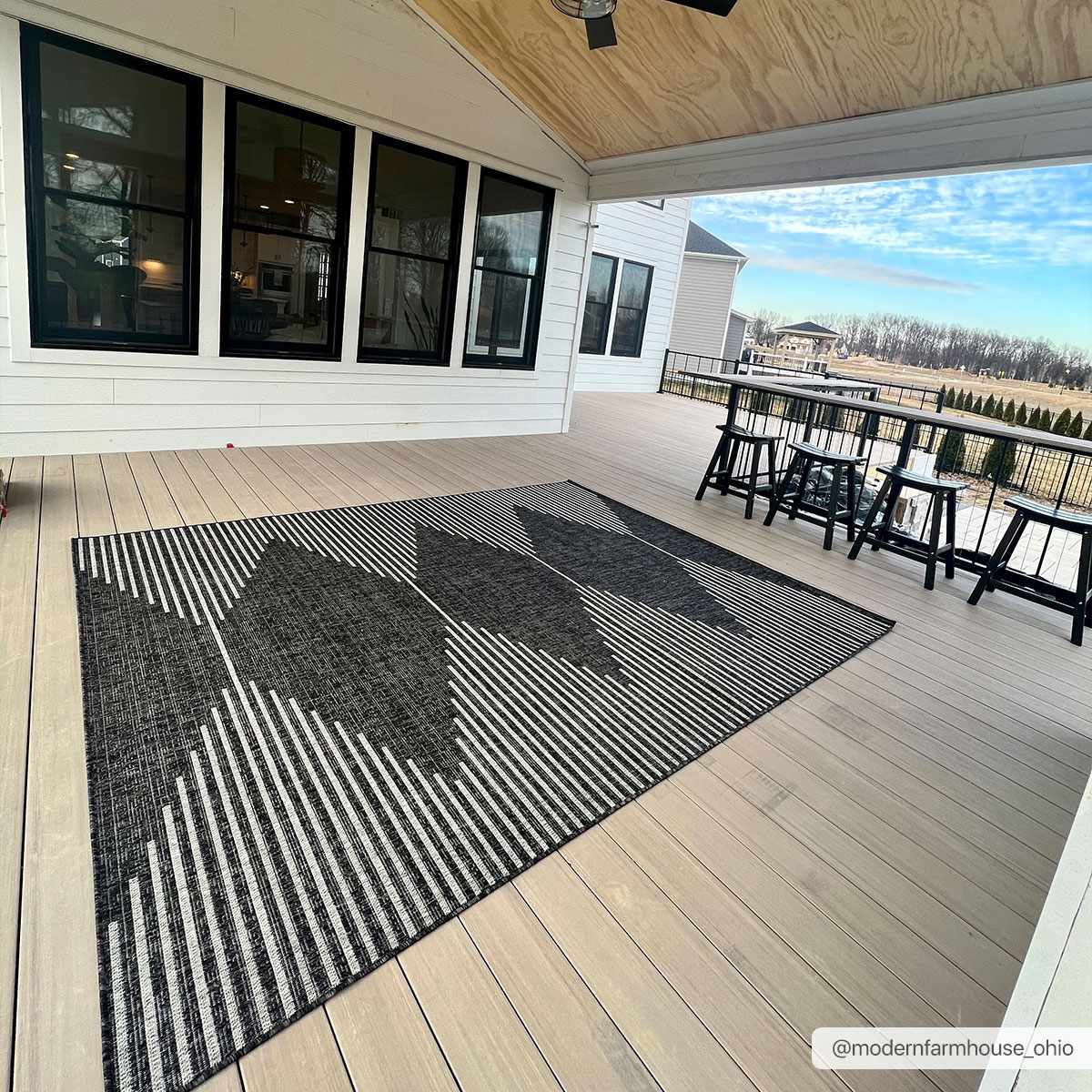 Black and white patterned rug on a wooden deck with a house and outdoor furniture in the background.