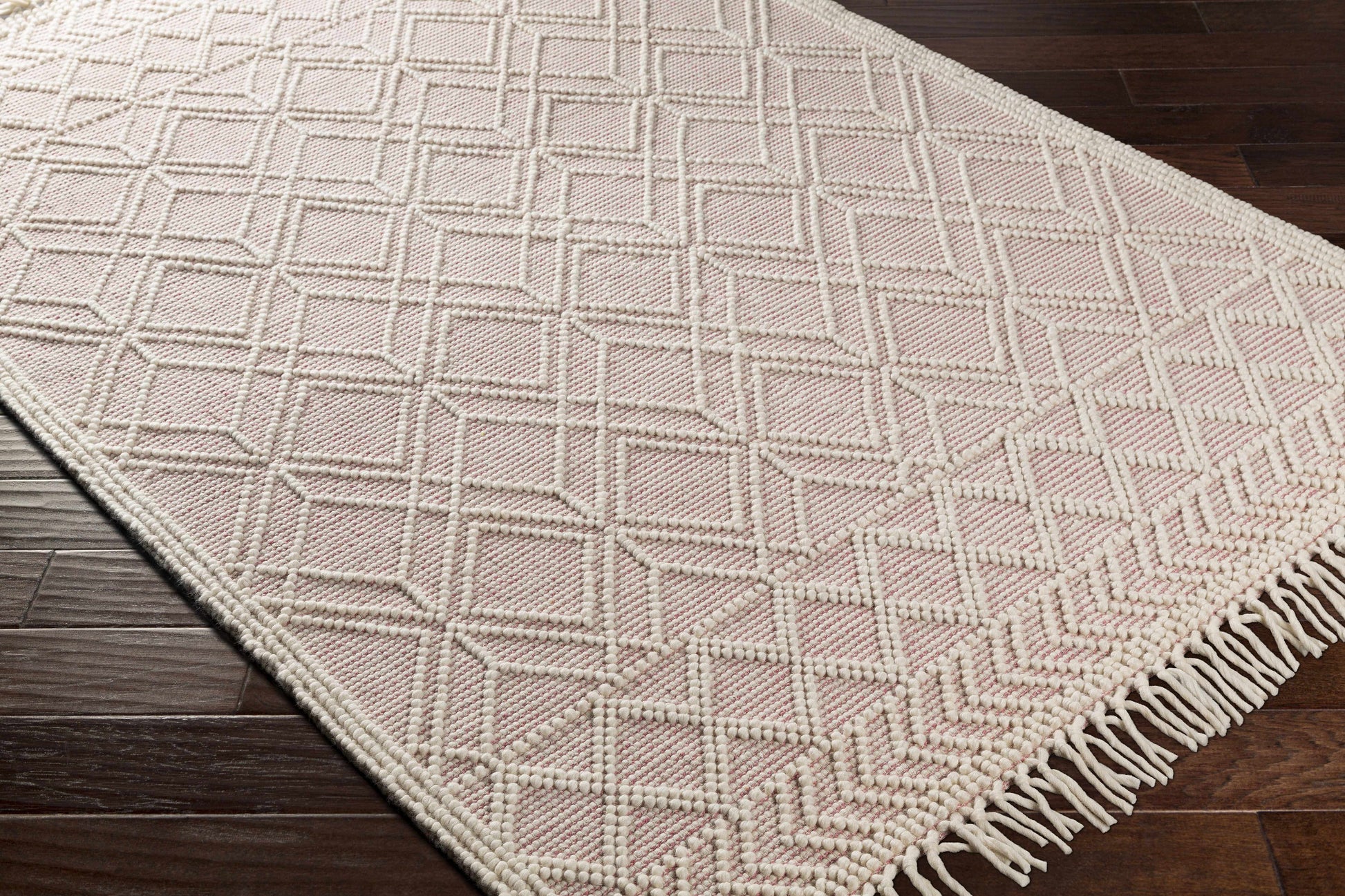 Pink geometric patterned rug with white fringe on a wooden floor