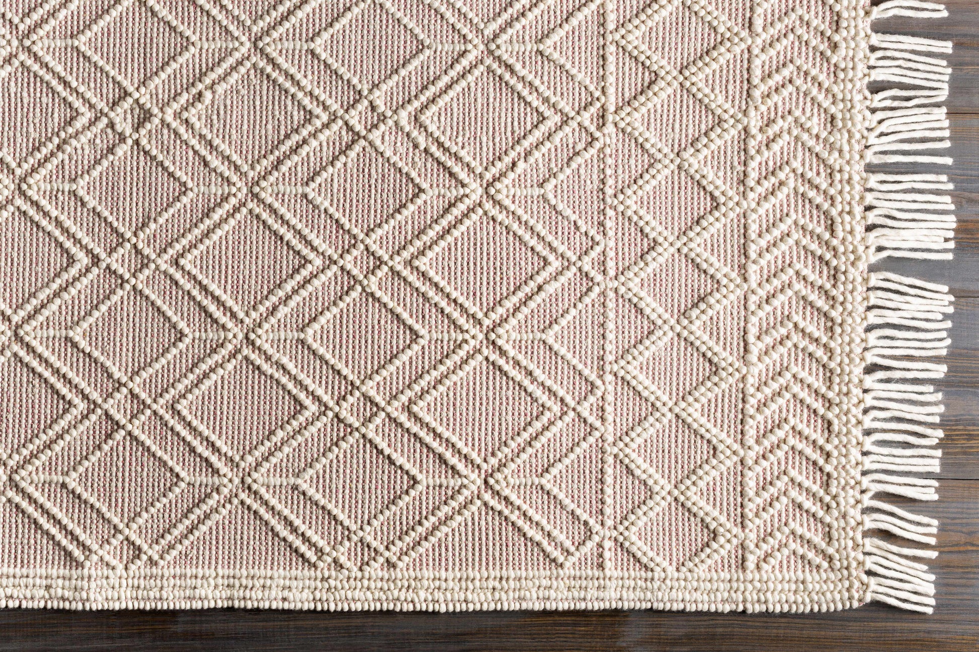 Pink woven rug with geometric pattern and tassels on a wooden floor
