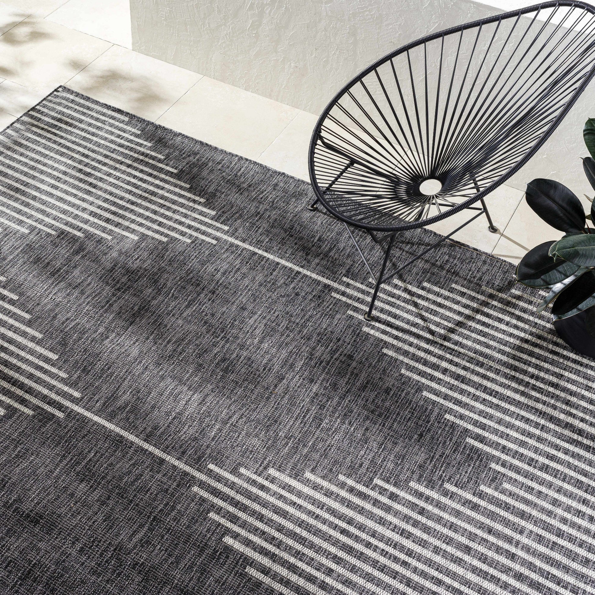 Patterned gray rug with a black wire chair on a white floor.