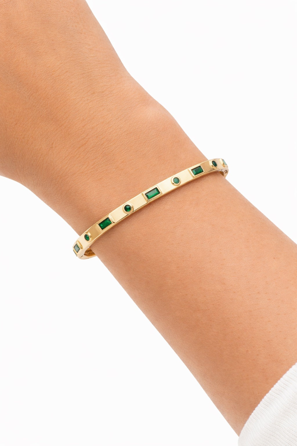 Emerald bezel gold bangle bracelet worn on wrist